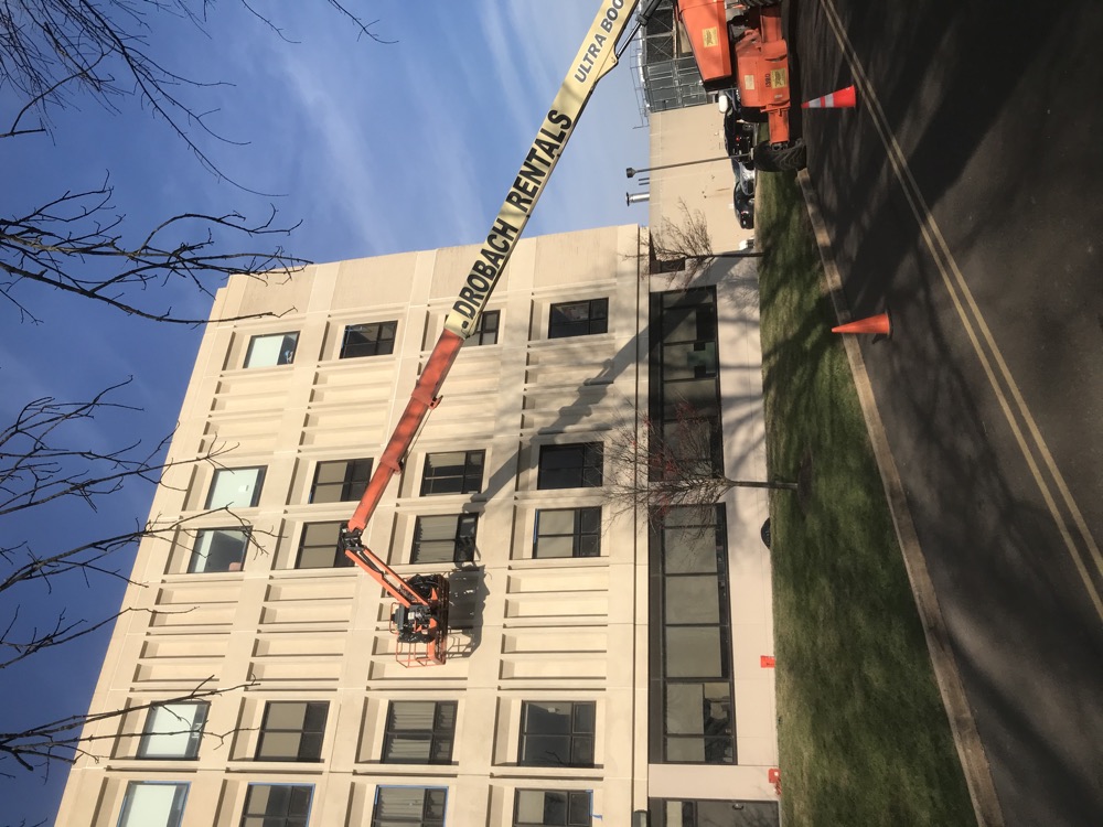 Boom lift positioned against a multi-story institutional building during exterior facade work